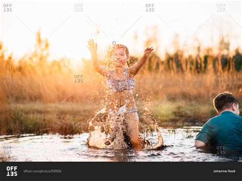 Girl splashes water in mud puddle with brother stock photo - OFFSET