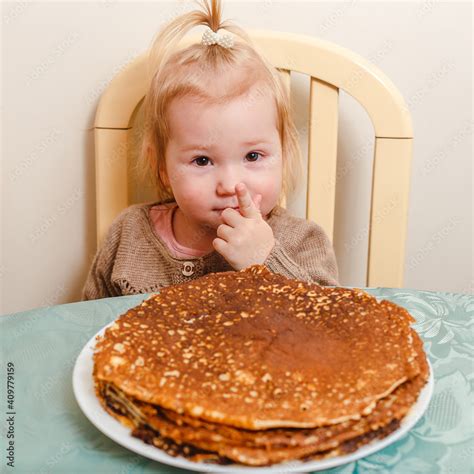 beautiful little girl sits at a table with large round pancakes. Carnival festival. Stock Photo ...