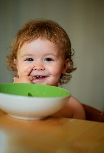 Premium Photo | Funny baby eating food himself with a spoon on kitchen ...