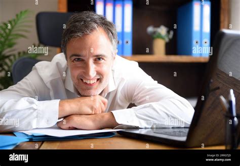 Business entrepreneur man in white shirt smiling and leaning on an office table with documents ...