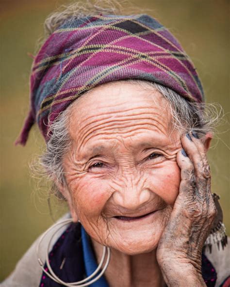 an old woman smiles while holding her hands to her face