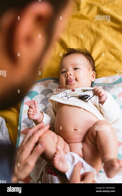 vertical shot of baby during diaper change by young father in bed. changing diaper to baby ...