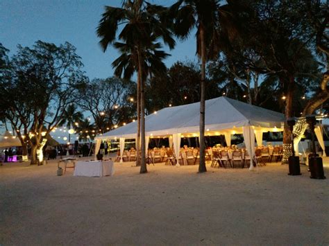 a tent set up with tables and chairs under palm trees on the beach at night