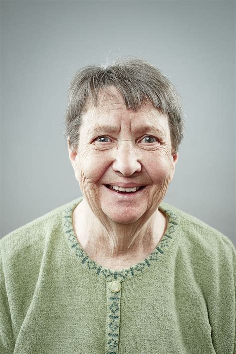 an older woman with gray hair and green shirt smiling at the camera while wearing a cardigan