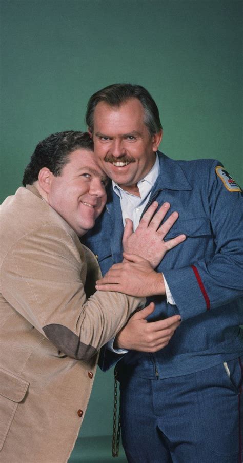 two men are hugging each other in front of a green background and one is wearing a blue suit