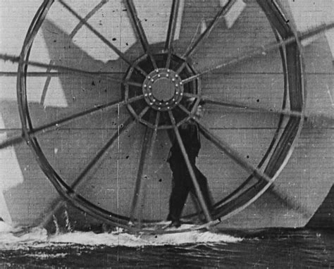 a man standing in front of a large wheel on top of the ocean next to ...