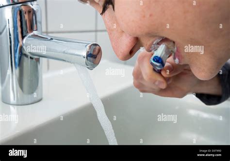 Woman is brushing her teeth, while water is still running from the tap. Symbol image for water ...