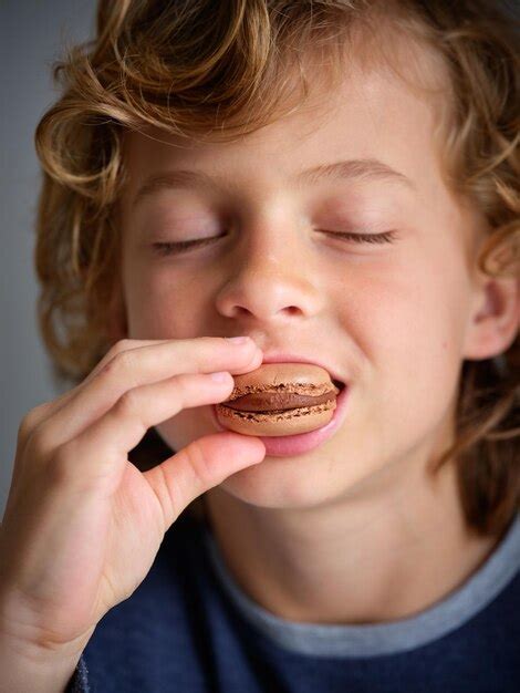 Premium Photo | Cute boy with curly hair and closed eyes eating tasty freshly baked chocolate ...