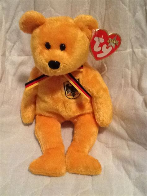 a yellow teddy bear sitting on top of a white sheet with a heart shaped tag