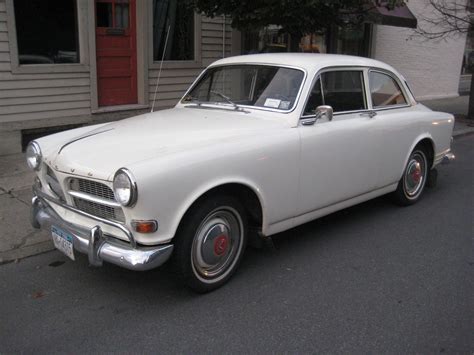 an old white car is parked on the side of the road in front of a house