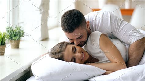 Young beautiful and loving couple wake up at the morning. Attractive man kiss and hug his wife ...