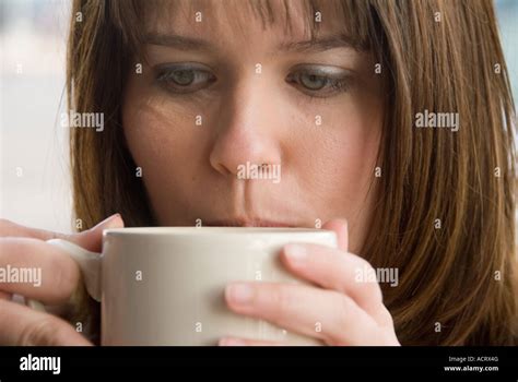 A young woman sips her coffee and talks on the phone as she relaxes in a small coffee shop ...