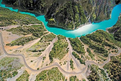 an aerial view of a winding road in the middle of a mountain range with blue water