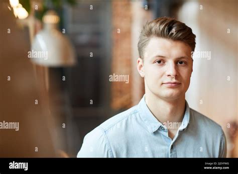 Portrait of serious young successful entrepreneur with stylish hairstyle standing in modern cafe ...