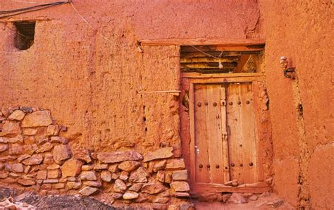 The old house wall, built partly of stone and earthen brick and covered with reddish adobe ...