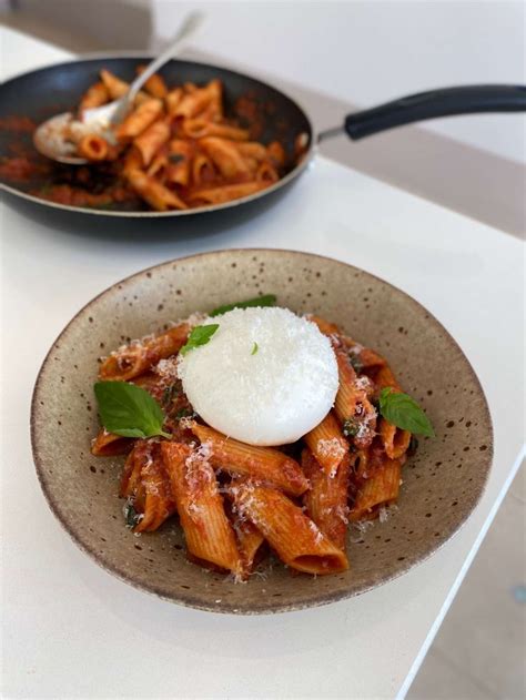 two plates of pasta with sauce, cheese and basil on the table next to ...