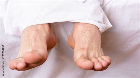Man sleeping on bed under blanket. Sleep alone. Healthy skin on foot. Size of foot. Male feet on ...