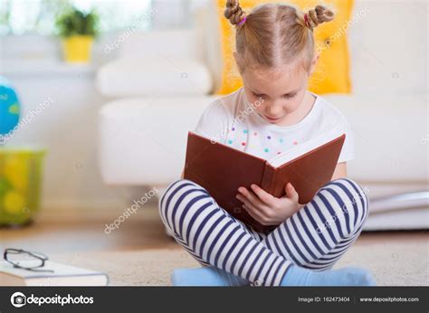 Portrait of clever little girl sitting with book on the floor Stock ...