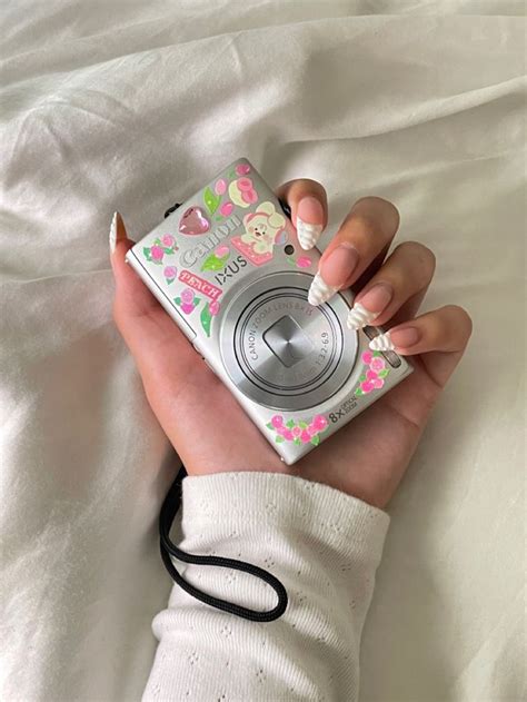 a person holding a camera in their hand with white and pink flowers on ...