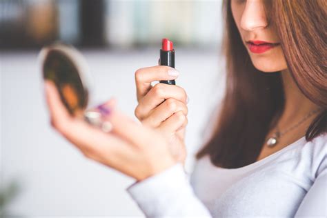 Woman with brown hair doing lipstick and holding little mirror · Free Stock Photo