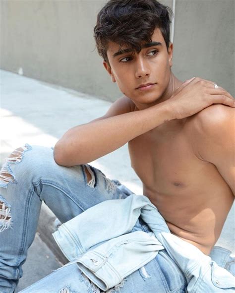 a shirtless young man sitting on the ground with his hand on his chest and looking at the camera