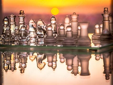 Reflected glass chess pieces with a saturated orange and yellow colored solar circle sunset in ...