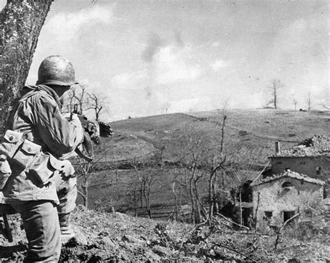 An American infantryman approaching an Italian house with caution and his BAR M1918A2 at his ...