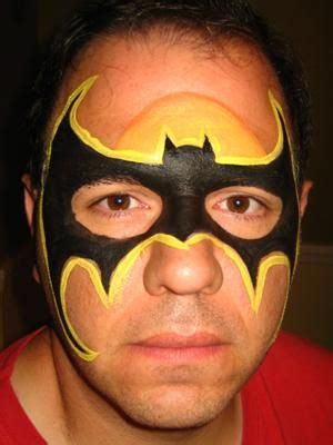 a man wearing a batman mask with yellow and black paint on his face is looking at the camera