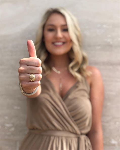 a woman giving the thumbs up sign in front of a white wall wearing a tan dress