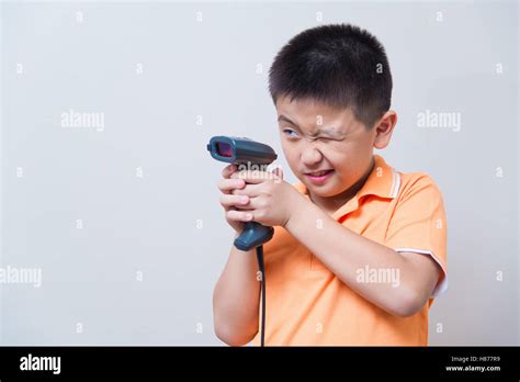 Asian boy aim a fake gun made with barcode scanner, studio shot, on gray wall background with ...