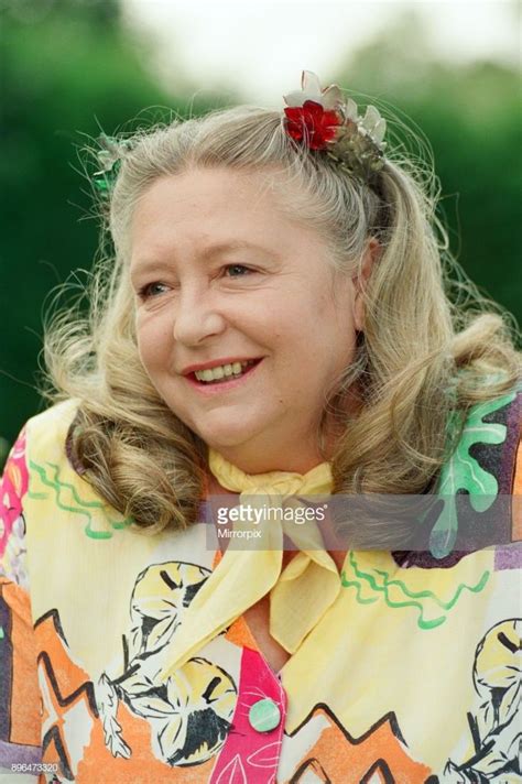 an older woman with blonde hair wearing a colorful shirt and flower in her hair, smiling at the ...