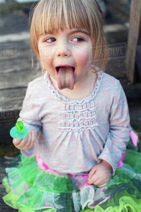 Young girl sticking out tongue after sucking on green ring candy; Toronto, Ontario, Canada ...