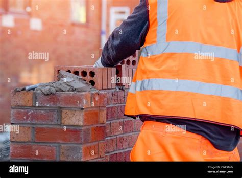 Hard working bricklayer lays bricks on cement mix on construction site. Fight housing crisis by ...