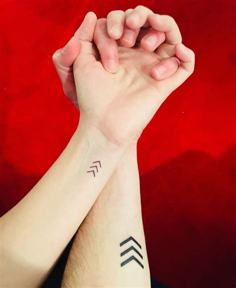 two people holding hands with tattoos on their wrists and armbands, both showing arrows