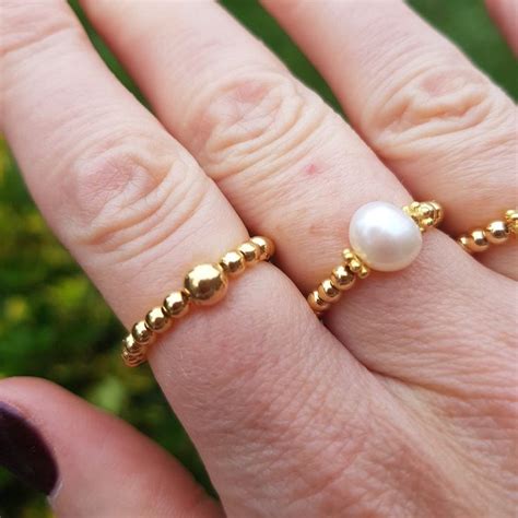 a woman's hand with a gold ring and a white pearl bead on it