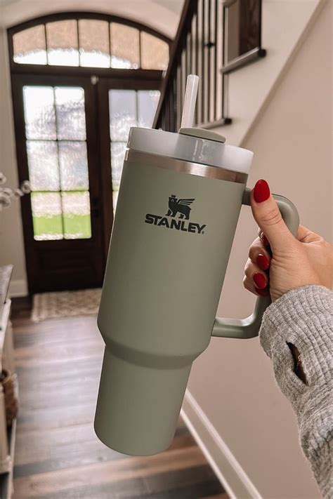 a woman holding a coffee cup in her hand while standing next to stairs with the name stanley on it