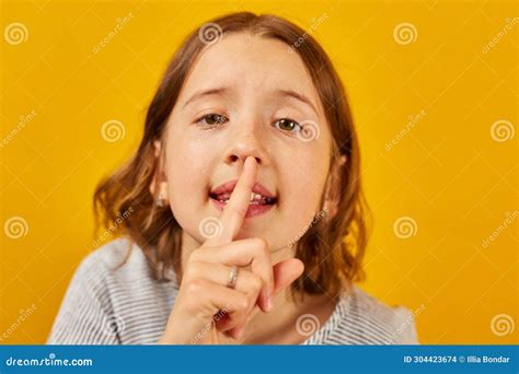 Young Girl Gesturing Silence with Finger on Lips Against Bright Yellow Background Stock Photo ...