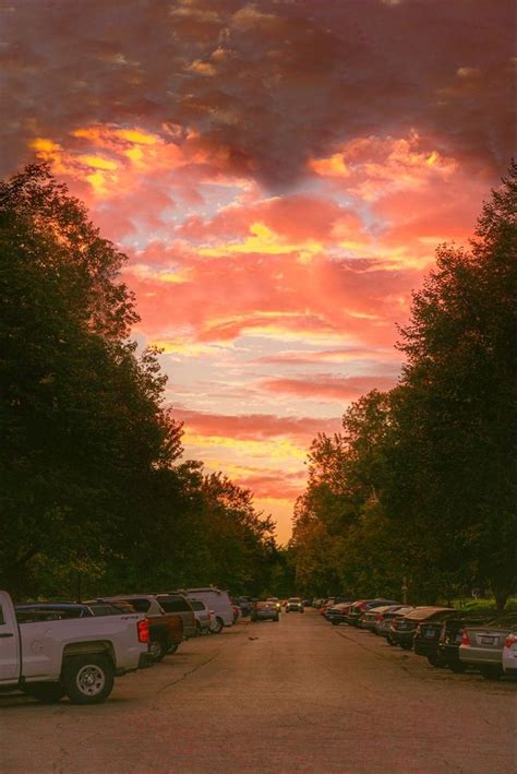 a parking lot filled with lots of parked cars under a colorful sky at sunset or sunrise