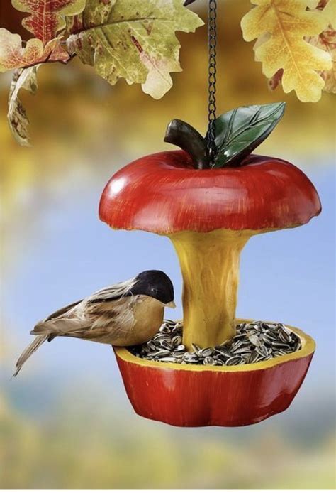 a bird sitting on top of a red apple shaped bird feeder hanging from a chain