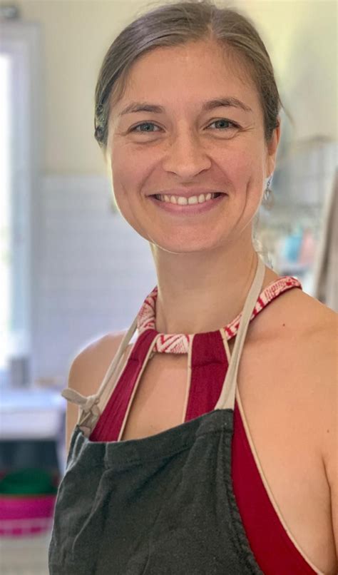 a woman in an apron smiling at the camera while wearing a red and gray top