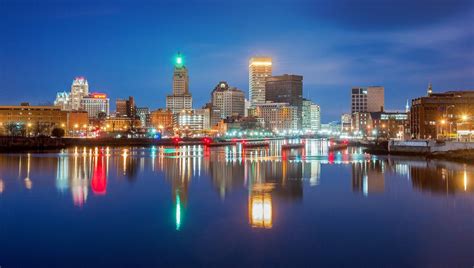 the city skyline is lit up at night with lights reflecting in the water and buildings