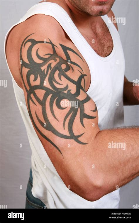 Closeup of muscular male bicep and shoulder with green tattoo body art branding on young 20's ...