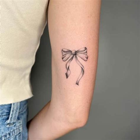 a woman's arm with a bow tattoo on the left side of her arm