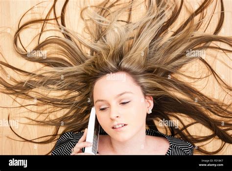 Head and shoulders, blonde teenage blue eyed girl laying on wood floor talking on phone. Hair ...
