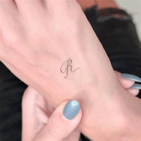 Little letter "R" tattoo located on the hand.