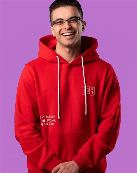 a man in a red hoodie smiles at the camera with his hands on his hips