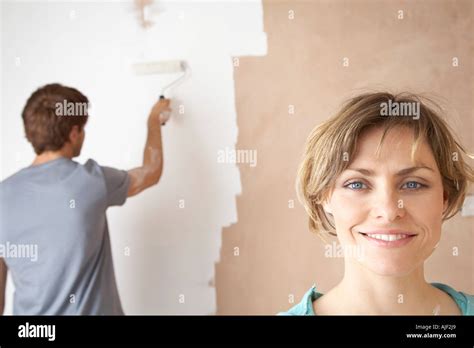 Woman smiling while man roller paints interior wall Stock Photo - Alamy