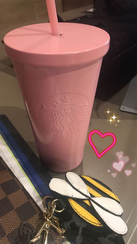 a pink starbucks cup sitting on top of a table next to other items and a keychain