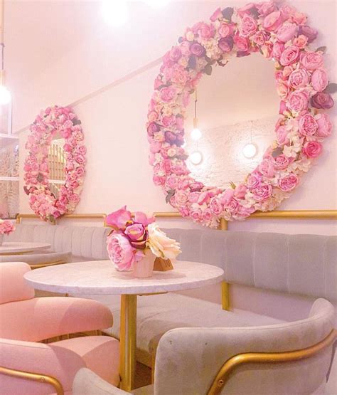 pink chairs and tables in a room with flowers on the wall, mirrors above them