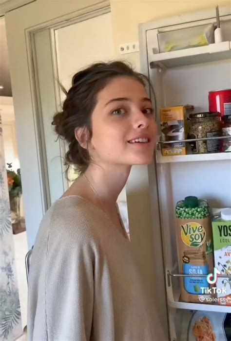 a woman standing in front of an open refrigerator with food on the shelves and she is smiling